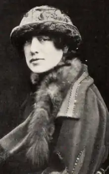 A white woman wearing a brimmed fabric hat, a fabric coat, and a fur stole