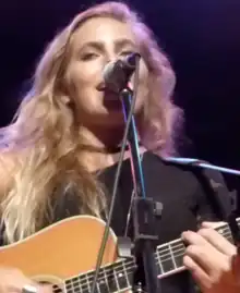 Singer Lauren Jenkins singing into a microphone while playing the guitar.