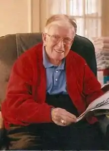 Photo of an elderly Monahan sitting in a chair and reading a newspaper