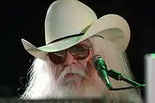 Musician Leon Russell is shown from the head up in front of a microphone.
