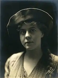 A young white woman photographed in high contrast with overhead light; her hat's brim is bright, and her face is mostly in shadow.