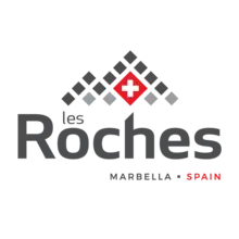 The words 'Les Roches, Marbella, Spain' are topped by black and gray squares arranged into the shape of mountains. The Swiss flag--a white cross on a red background--is at the heart of the mountain.