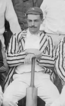A blackened white portrait of a cricketer, seated holding a cricket bat