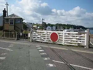 Level crossing gates against a railway track over a minor road. A yellow and green signal box is on the left behind the gate