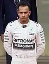 Lewis Hamilton in silver racing overalls standing on the third spot on the podium