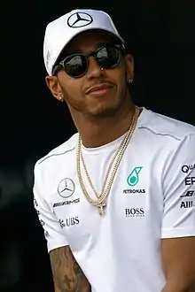 Lewis Hamilton wearing a silver baseball cap and T-shirt with black sunglasses and a necklace around his neck