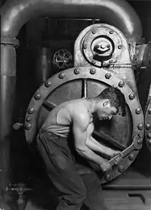 Image 42Lewis Hine's 1920 image "Power house mechanic working on steam pump," which shows a working class young American man with wrench in hand, hunched over, surrounded by the machinery that defines his work.