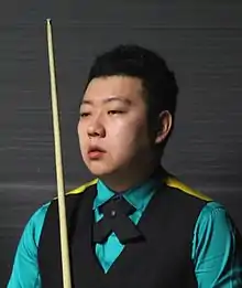 A Chinese man sat down holding a snooker cue