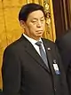 a grumpy looking man looking downwards, wearing white shirt, a suit and a blue tie