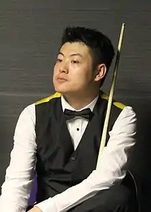 A Chinese man sat down holding a snooker cue