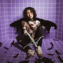 Lil Lotus, wearing bandages and shredded black wings, holding a crossbow while sitting on the floor of a purple-tiled room