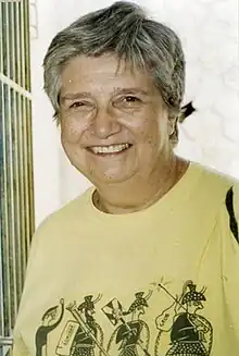 A grey-haired woman, facing the camera, in a t-shirt with a cartoon of the Warrior Vase from Mycenae.