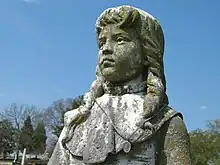 Grey stone statue of a 12-year-old girl with shoulder-length hair.