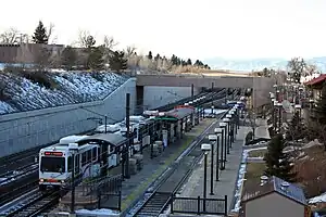 A white train is parked at a recessed island platformed station with canopies and lighting visible.