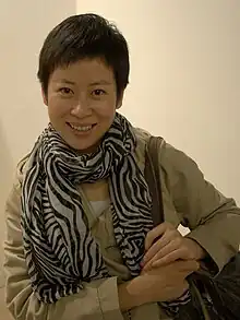 An Asian woman with short cropped hair smiling at the camera, wearing a zebra-stripe scarf