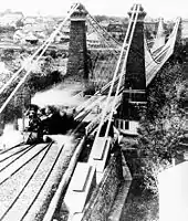 Three railway lines merge into one, crossing a bridge. A train engine has crossed the bridge and is moving into the left-most line.