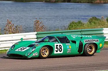 A picture of a green racing sports car on a track with a lake in the background