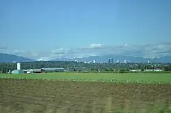 Farm fields, with South Slope, Burnaby, and the Metrotown skyline in the distance.