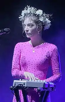 A picture of Lorde on stage wearing a pink dress and flower crown as plays a MIDI controller.