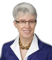 A photographic portrait of a middle-aged woman from the shoulders up, wearing a suit and eyeglasses