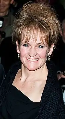 Colour photograph of Lorraine Asbourne. She is looking into the camera, smiling. She is wearing a black dress.