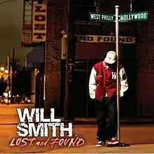 An image of a man wearing black jeans, a red and white varsity jacket, hat and sneakers, standing next to a directional street sign that point to "West Philly" and "Hollywood".