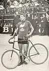 A man in a cycling uniform standing beside his bicycle on a racetrack
