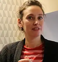 close-up of Louise Coldefy wearing a striped red and pink top and a dark jacket, grinning directly at camera