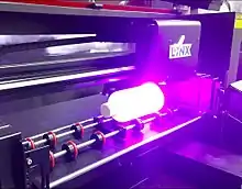 A Lynx ULTRA 64 flatbed UV printer with a rotary attachment printing on a bottle.