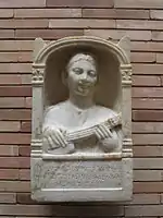 Memorial stele for a 16-year-old Roman woman, depicted playing a pandura-type instrument, date estimated 2nd century A.D. Unearthed in 1956 at the archeological site Emerita Augusta in Spain. Kept at the Museo Nacional de Arte Romano in Mérida, Spain.