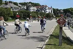 Bicyclists on a road. Houses can be seen at left.