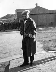 A gunmen, later identified as M. Lopez, standing holding a partially lowered long barrel gun looking at the camera