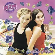 Two teenage girls, one blonde and one brunette, sitting on a bed in front of a purple wall. The girls are surrounded by watermarks of violets. 'M2M' appears in the upper left corner and 'Shades of Purple' appears in the bottom right.