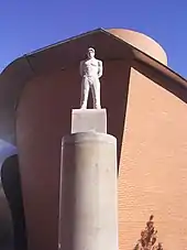 A stone statue of Shakur standing on a tall stone pillar in front of the MARTa Herford museum
