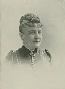 B&W portrait photo of a middle-aged women with blonde hair in an up-do, wearing a dark blouse.