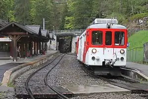 Boxy red-and-white train on double-track railway line next to station