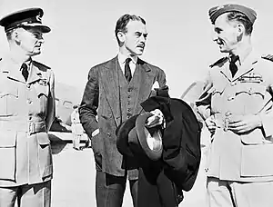 Mustachioed man in business suit flanked by two men in military uniforms