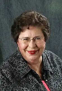 An older white woman, with dark hair, wearing glasses.