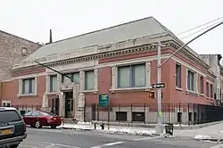 A square two-story brick building stands before a snowy sidewalk against a gray sky.