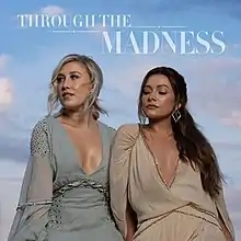 A photograph of the duo sat next to eachother, bodies facing forward but faces pointed off to the left. Maddie is wearing a blue-grey dress and has her eyes open, while Tae's eyes are closed and she's wearing a light brown dress and diamond-shaped earrings. The background is of a midday blue sky covered in white clouds, and the name of the release is printed across the top of the frame.