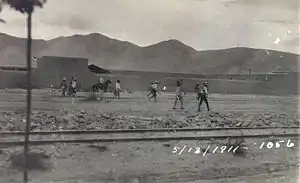 A group of men wearing sombreros walking along a dirt road between a railroad track and a line of buildings.  Dated 5/13/1911.