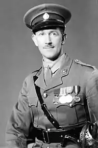 A half-length studio portrait of a man in military uniform. He is wearing an officer's cap, and has four medals on his breast.
