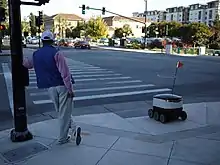 Image 11A man and a delivery robot waiting at a pedestrian crossing in Redwood City, California, United States. E-commerce spurred advancements in drone delivery and transformed parts of the services and retail sectors (from 2010s)