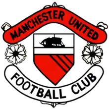 A football crest. In the centre is a shield with a ship in full sail above a red field with three diagonal black lines. Either side of the shield are two stylised roses, separating two scrolls. The upper scroll is red and reads "Manchester United" in black type, while the lower scroll is white with "Football Club" also written in black