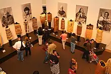 Museum goers look an exhibit of clothing from New Zealand's Toi Maori people. On the wall behind are photos of individuals wearing examples of the clothing.