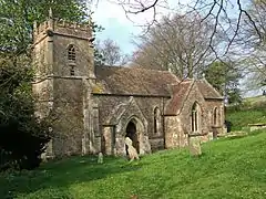 Yellow stone building with square tower, surrounded by trees.