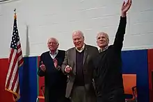 Three older men on a stage next to an American flag. (from Vermont)