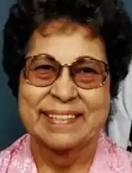 A smiling older Native American woman wearing glasses and a pink shirt