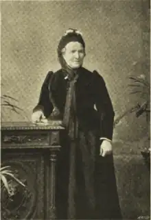 portrait of an old woman, standing up, wearing dark clothing