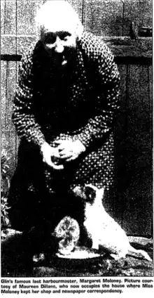 Very poor resolution photo of an older woman, hunched over. There small dog sitting beside her.